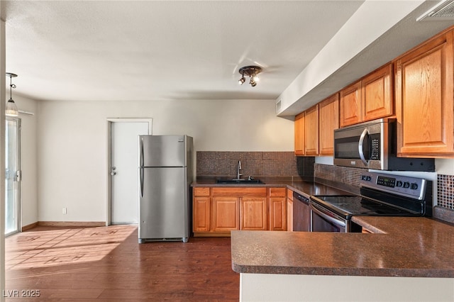 kitchen featuring dark wood finished floors, dark countertops, appliances with stainless steel finishes, a sink, and a peninsula