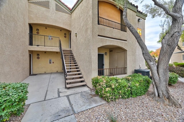 property entrance featuring a balcony, a tiled roof, central air condition unit, a patio area, and stucco siding