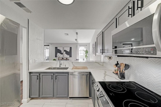 kitchen with light stone counters, gray cabinetry, a sink, visible vents, and appliances with stainless steel finishes