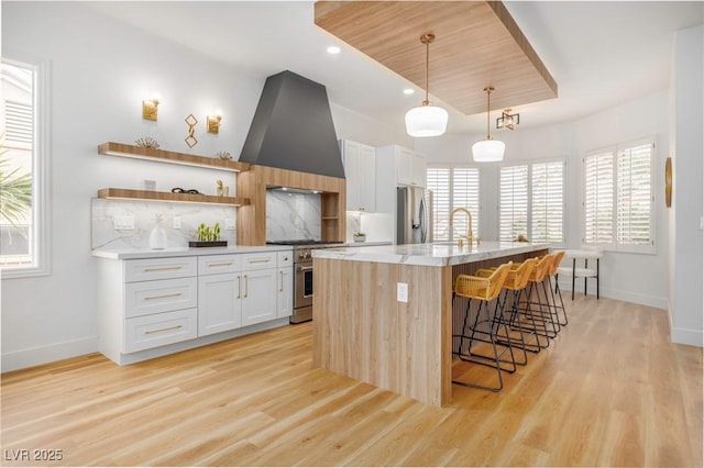 kitchen with appliances with stainless steel finishes, premium range hood, light wood-style floors, and a kitchen breakfast bar