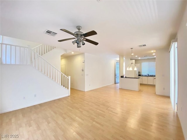 unfurnished living room featuring light wood-style flooring, stairs, visible vents, and a ceiling fan