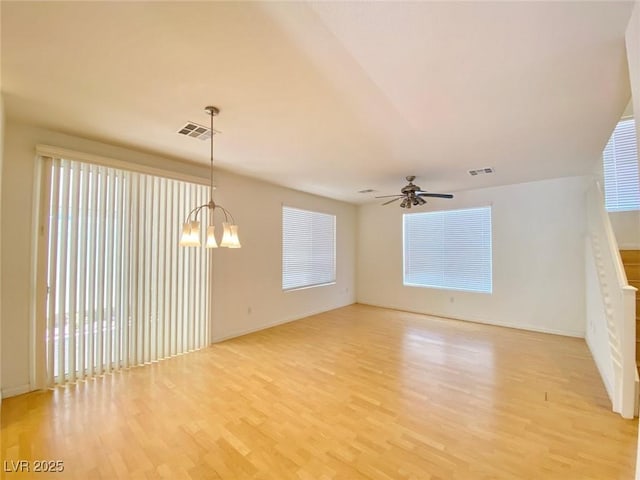 spare room with light wood-type flooring, plenty of natural light, visible vents, and ceiling fan with notable chandelier