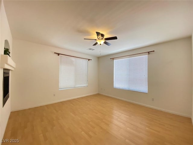 spare room featuring baseboards, a ceiling fan, and light wood-style floors