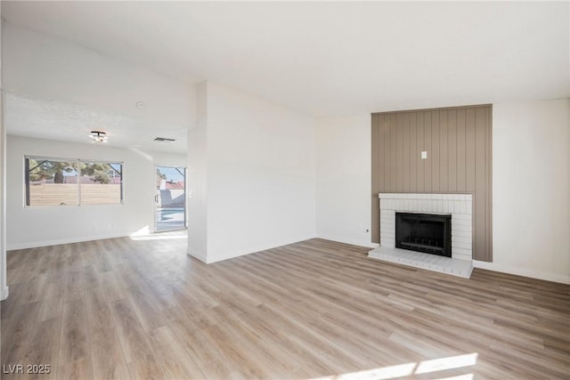 unfurnished living room featuring light wood-style floors, a brick fireplace, and baseboards