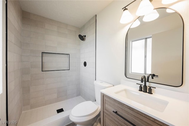 bathroom with toilet, tiled shower, and vanity