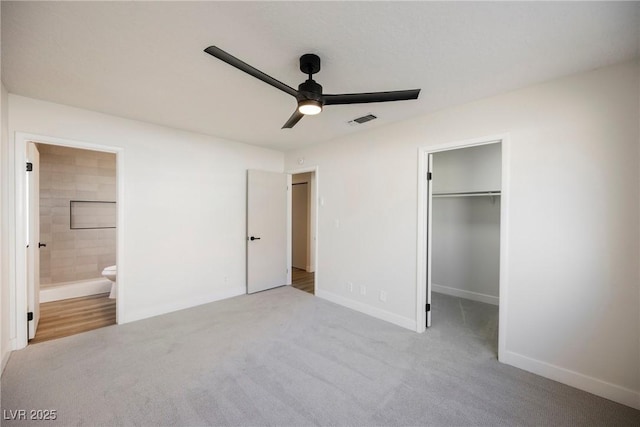 unfurnished bedroom featuring connected bathroom, carpet flooring, visible vents, baseboards, and a walk in closet