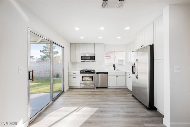 kitchen featuring visible vents, white cabinets, stainless steel appliances, light countertops, and light wood-type flooring