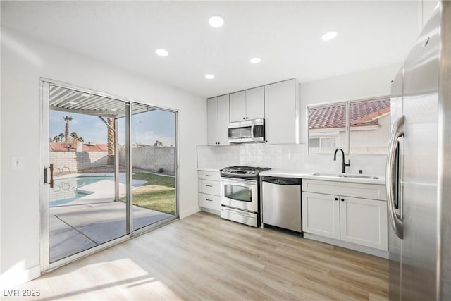 kitchen featuring a sink, light countertops, appliances with stainless steel finishes, light wood finished floors, and tasteful backsplash