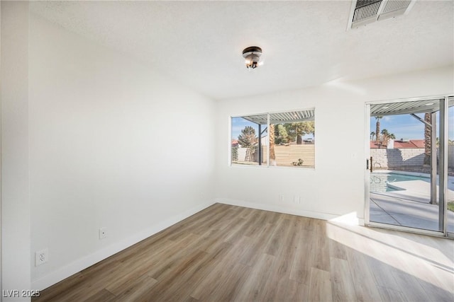 empty room featuring visible vents, plenty of natural light, baseboards, and wood finished floors