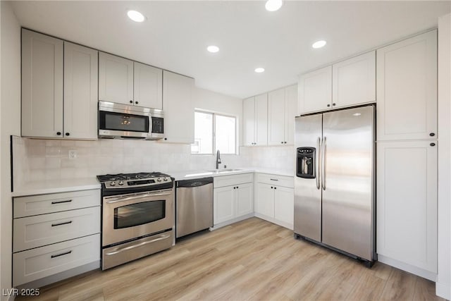 kitchen with a sink, light wood-style floors, light countertops, appliances with stainless steel finishes, and backsplash