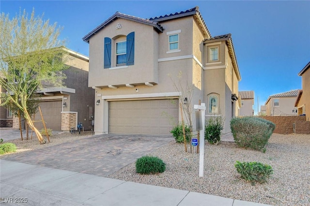 mediterranean / spanish home with decorative driveway, a tile roof, an attached garage, and stucco siding