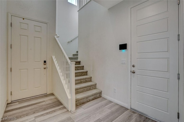 entryway with light wood-type flooring, baseboards, and stairs