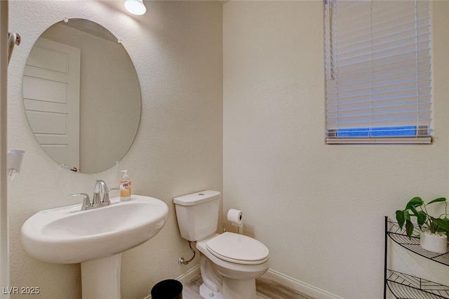 half bath with wood finished floors, toilet, and baseboards