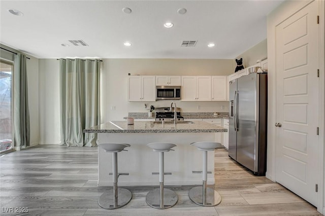 kitchen featuring appliances with stainless steel finishes, visible vents, an island with sink, and light stone counters