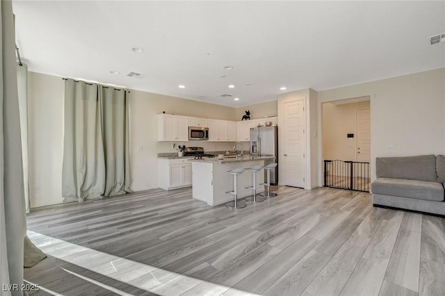 kitchen with white cabinets, appliances with stainless steel finishes, open floor plan, a kitchen breakfast bar, and a sink