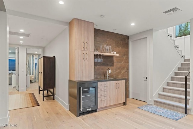 bar with beverage cooler, visible vents, wet bar, stairs, and a sink