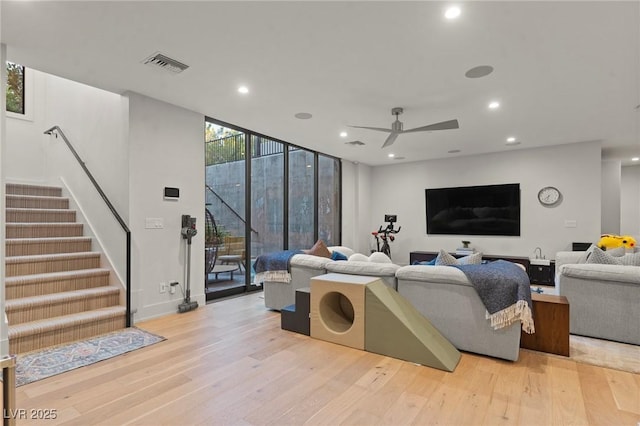 living room with light wood-style flooring, recessed lighting, visible vents, stairs, and expansive windows