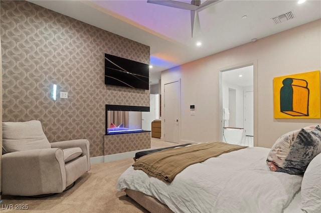 bedroom featuring light carpet, an accent wall, visible vents, baseboards, and wallpapered walls