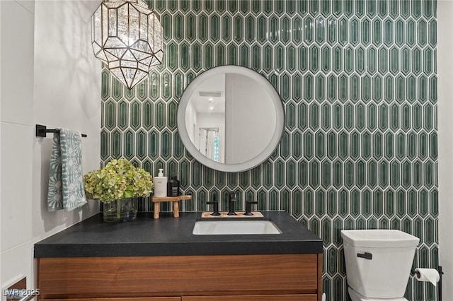 bathroom featuring a chandelier, vanity, toilet, and tile walls