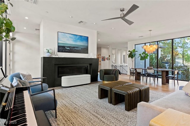 living area featuring recessed lighting, visible vents, wood finished floors, a fireplace, and ceiling fan with notable chandelier