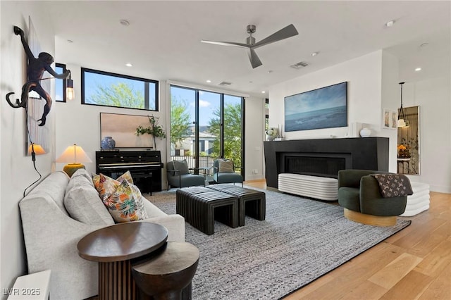 living room with recessed lighting, a fireplace, wood finished floors, visible vents, and floor to ceiling windows