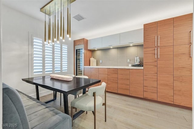 kitchen with beverage cooler, visible vents, light countertops, light wood finished floors, and tasteful backsplash