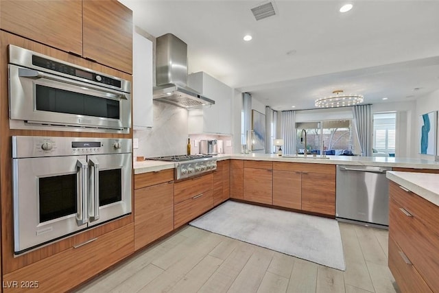 kitchen featuring stainless steel appliances, a sink, visible vents, light countertops, and wall chimney exhaust hood