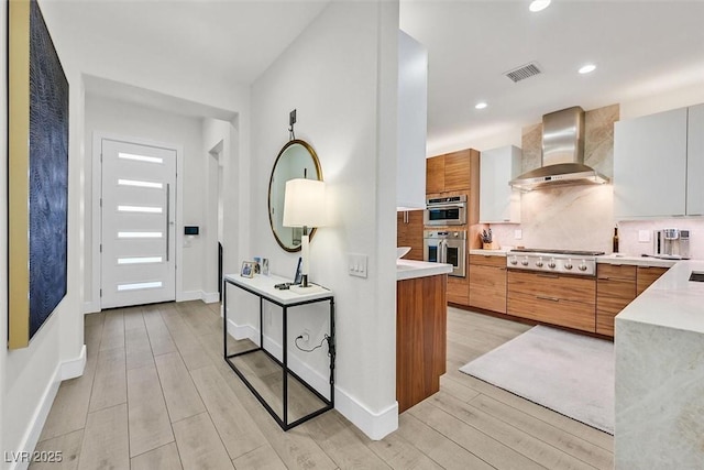 kitchen featuring stainless steel appliances, visible vents, light countertops, wall chimney range hood, and backsplash