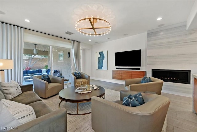 living area featuring a warm lit fireplace, visible vents, a chandelier, and wood finished floors