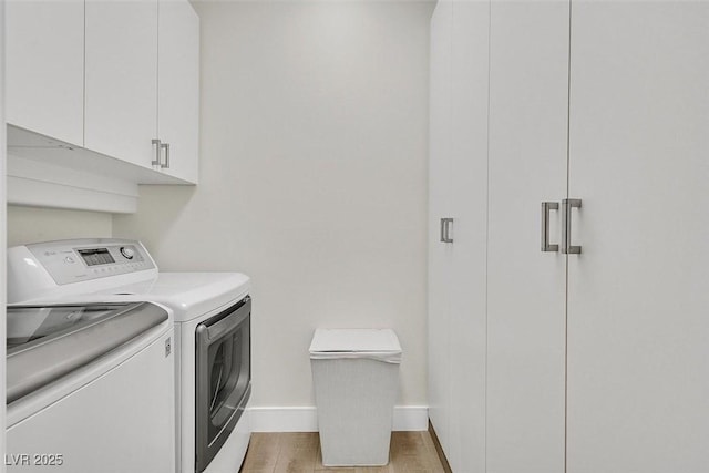 clothes washing area featuring light wood finished floors, washing machine and clothes dryer, cabinet space, and baseboards