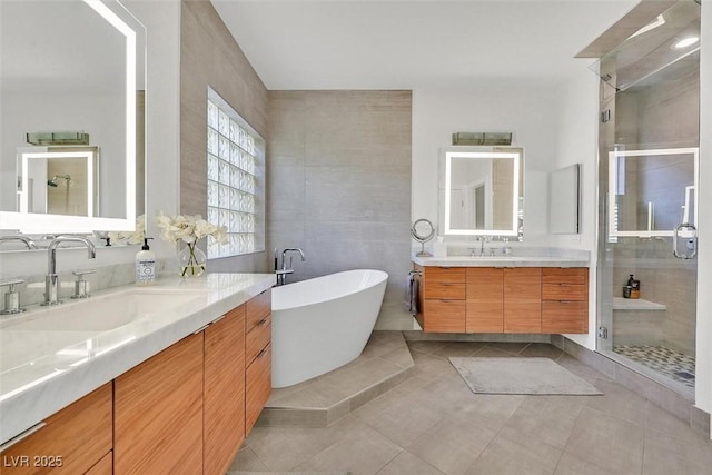 bathroom with two vanities, tile patterned floors, a sink, a shower stall, and tile walls