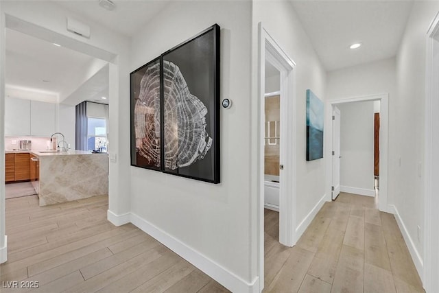 hall with recessed lighting, a sink, light wood-style flooring, and baseboards