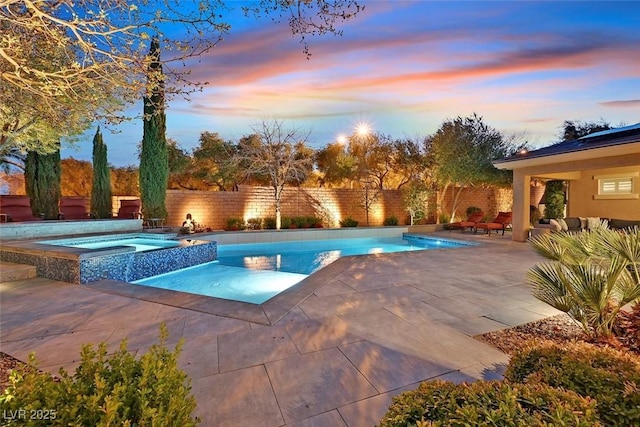 pool at dusk with a pool with connected hot tub, a patio area, and a fenced backyard