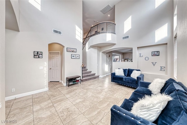 living room with arched walkways, visible vents, baseboards, and stairs