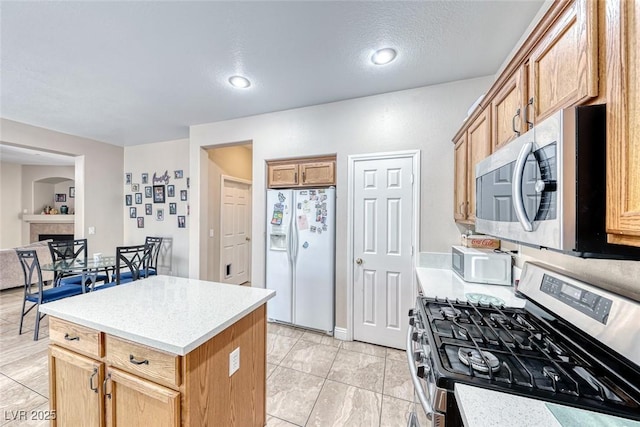 kitchen with a textured ceiling, a tile fireplace, stainless steel appliances, light countertops, and a center island