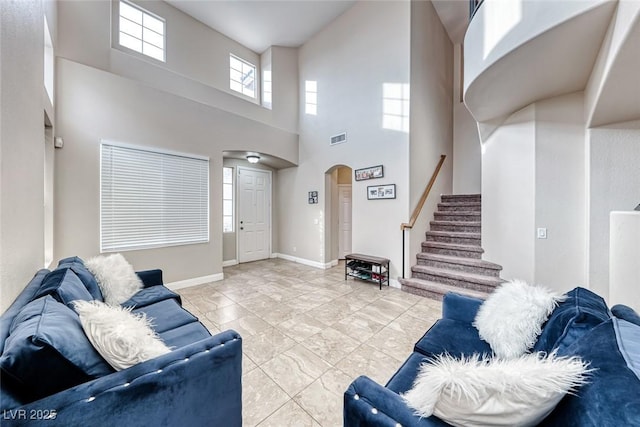 living room featuring arched walkways, a high ceiling, visible vents, baseboards, and stairway