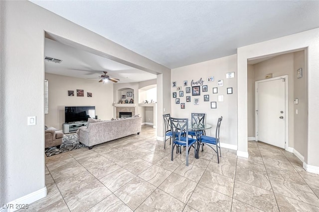 living area featuring a ceiling fan, visible vents, a fireplace, and baseboards