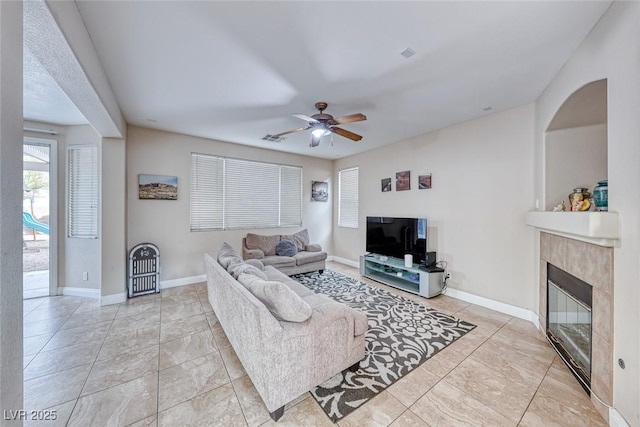 living room with a tile fireplace, a ceiling fan, and baseboards