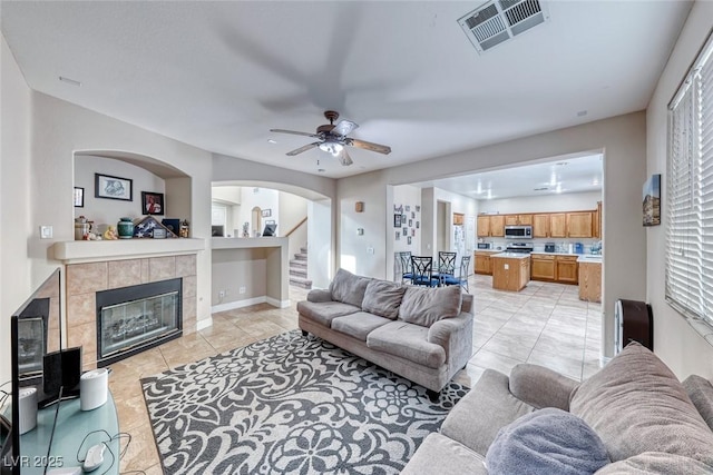 living room featuring ceiling fan, stairs, visible vents, and a tiled fireplace