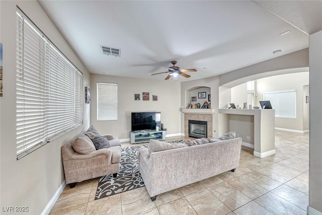 living area featuring a ceiling fan, visible vents, a tiled fireplace, and baseboards