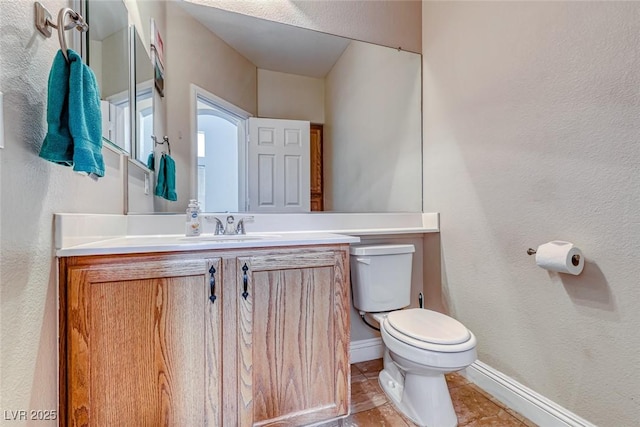 half bath with a textured wall, vanity, toilet, and baseboards