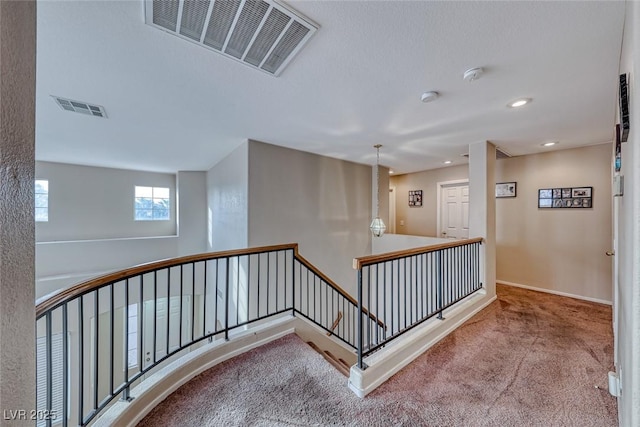 hall with carpet, baseboards, visible vents, and an upstairs landing