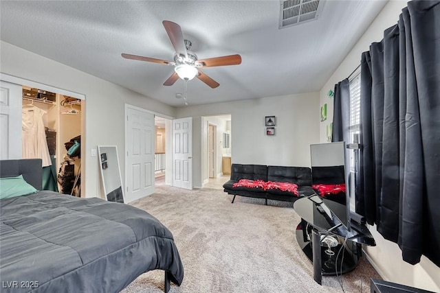 carpeted bedroom featuring a walk in closet, connected bathroom, visible vents, and a ceiling fan