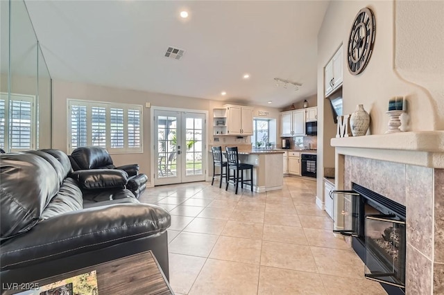 living room featuring light tile patterned floors, visible vents, a tile fireplace, lofted ceiling, and french doors