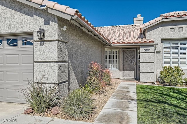 view of exterior entry featuring a garage, a tiled roof, a chimney, and stucco siding