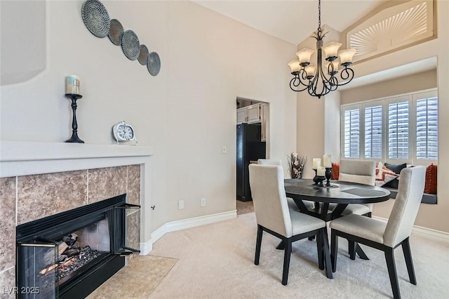 dining room featuring light carpet, baseboards, a chandelier, and a tile fireplace