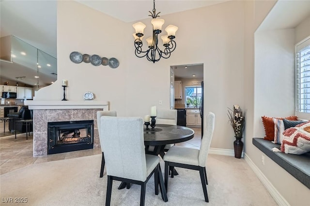 dining area with a fireplace, a high ceiling, an inviting chandelier, light carpet, and baseboards