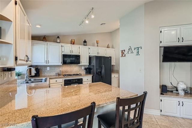 kitchen with light stone countertops, vaulted ceiling, black appliances, open shelves, and a sink