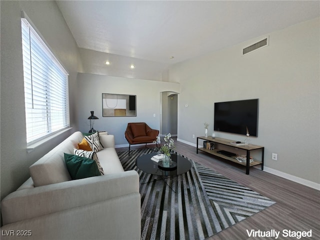 living area with arched walkways, wood finished floors, visible vents, baseboards, and vaulted ceiling