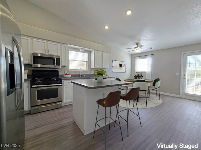 kitchen featuring white cabinets, a kitchen island, appliances with stainless steel finishes, a kitchen bar, and a sink